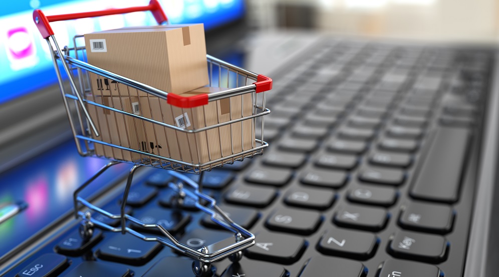 E-commerce. Shopping cart with cardboard boxes on laptop.